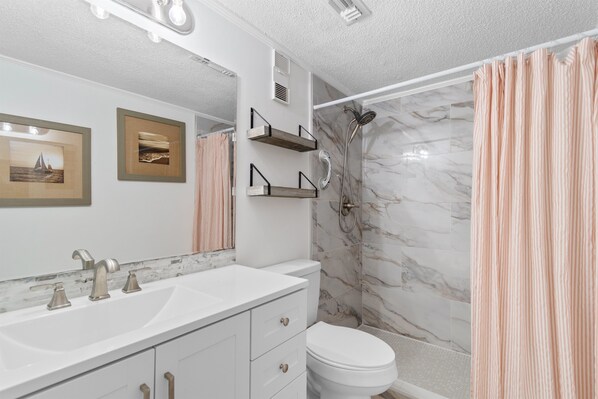A bathroom with a white vanity, a toilet, a shower with a marble wall, and a striped shower curtain.