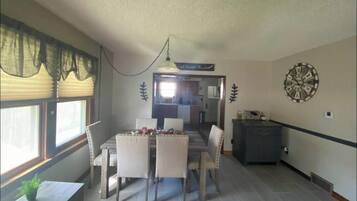 Un comedor con una mesa y sillas, un reloj en la pared y una ventana con persianas.