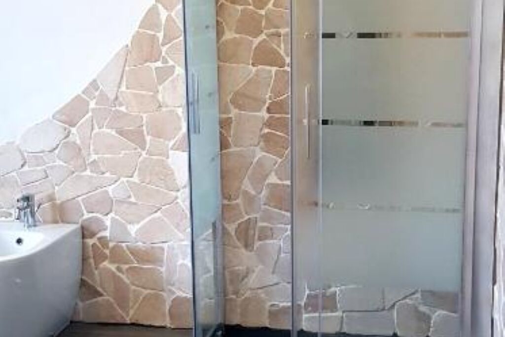 Une salle de bain avec un mur en pierre, un lavabo et une douche en verre.