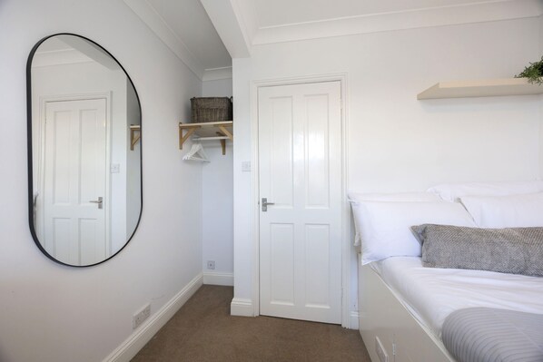 A bedroom with a bed, a white door, a mirror, and a shelf with baskets. - Spacious 3-Bed Period Home Near Bath Road (Cheltenham)