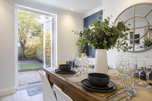 A dining area with a table set for six, a potted plant, and a view through a glass door to an outdoor garden.