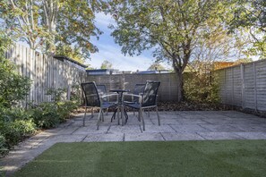 A patio with a table and chairs, surrounded by a wooden fence and trees. - Spacious 3-Bed Period Home Near Bath Road (Cheltenham)