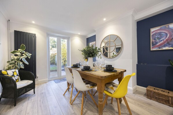 A dining area with a wooden table, white and yellow chairs, and a black and white patterned cushion.