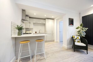 Une cuisine moderne avec des armoires blanches, une hotte de cuisinière en acier inoxydable et un coin bar avec des tabourets.