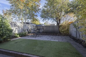 A backyard with a patio area, a wooden fence, and a tree. - Spacious 3-Bed Period Home Near Bath Road (Cheltenham)