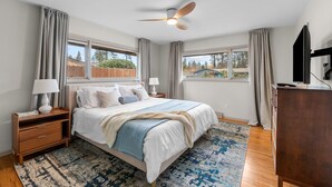 A bedroom with a bed, nightstands, a dresser, a ceiling fan, and large windows. - Stylish South Hill Getaway | Bar & Game Room (Spokane)