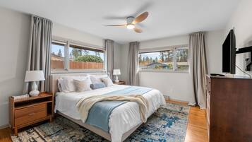 Une chambre à coucher comprenant un lit, des tables de chevet, une commode, un ventilateur de plafond et de grandes fenêtres.