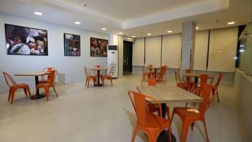 A dining area with tables and chairs, a television screen, and artwork on the walls.