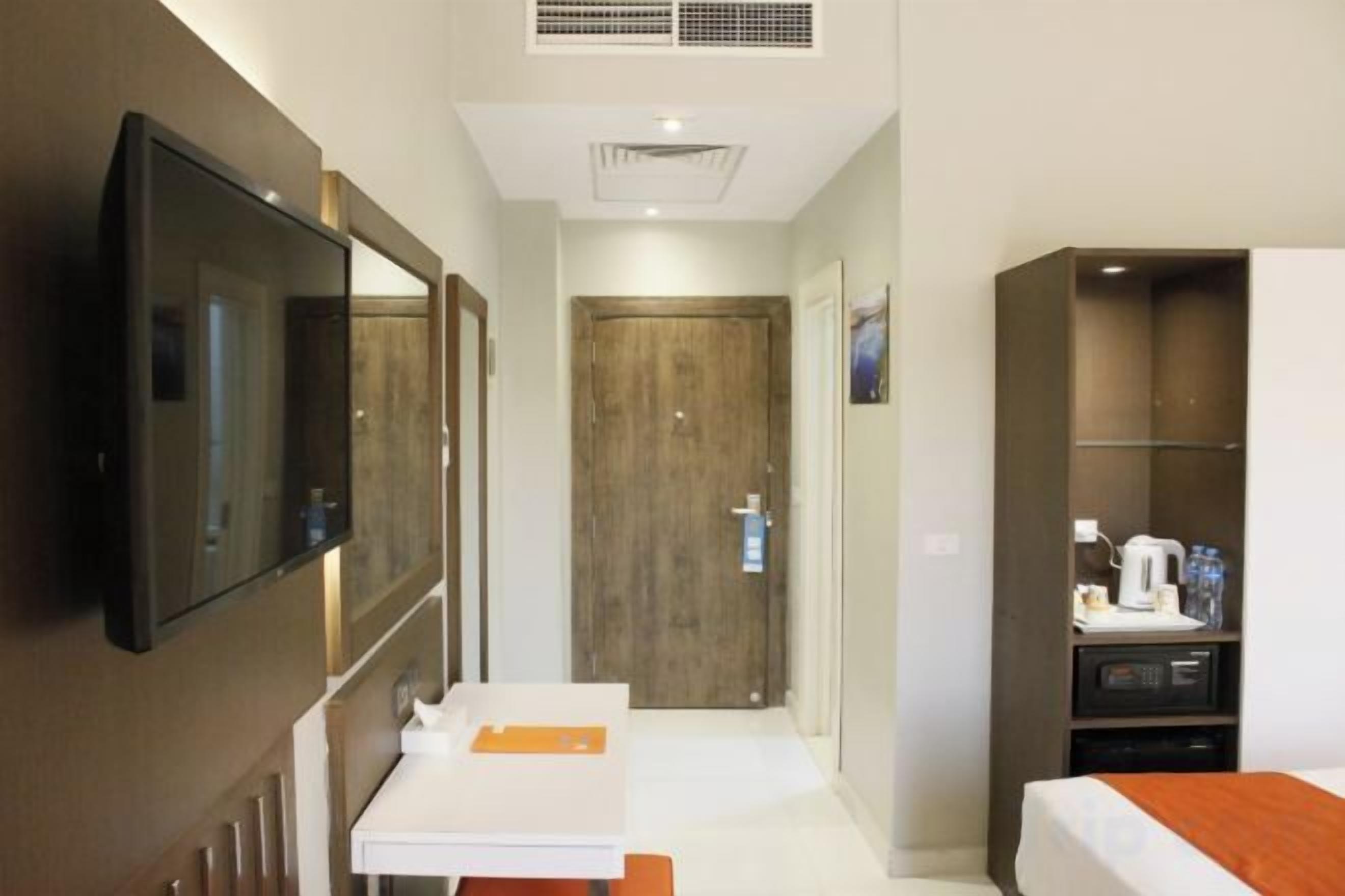 A hotel room with a TV, a wooden door, a white desk, and a bed.