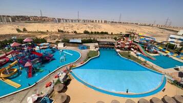 A water park with multiple slides and pools, surrounded by a sandy area and a clear sky.