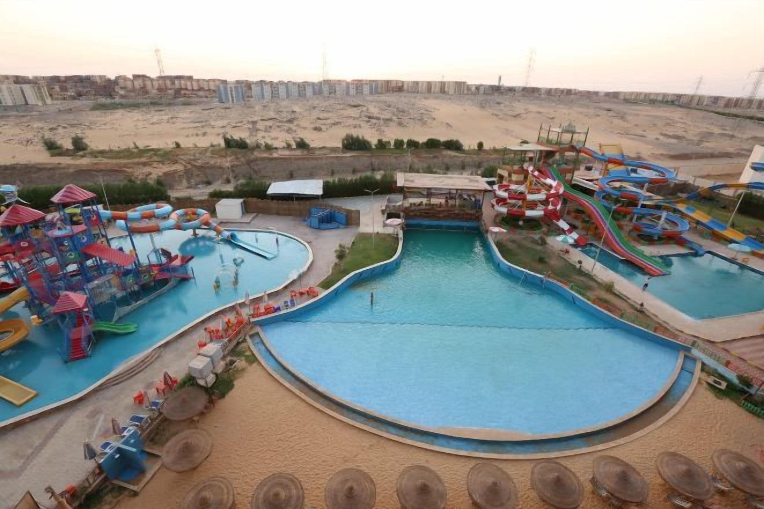 A water park with multiple pools and slides, surrounded by a sandy landscape.