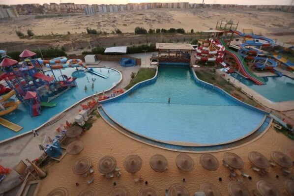 A water park with multiple pools and slides, surrounded by sandy areas and umbrellas. - Gloria Aqua Park (Aswan)