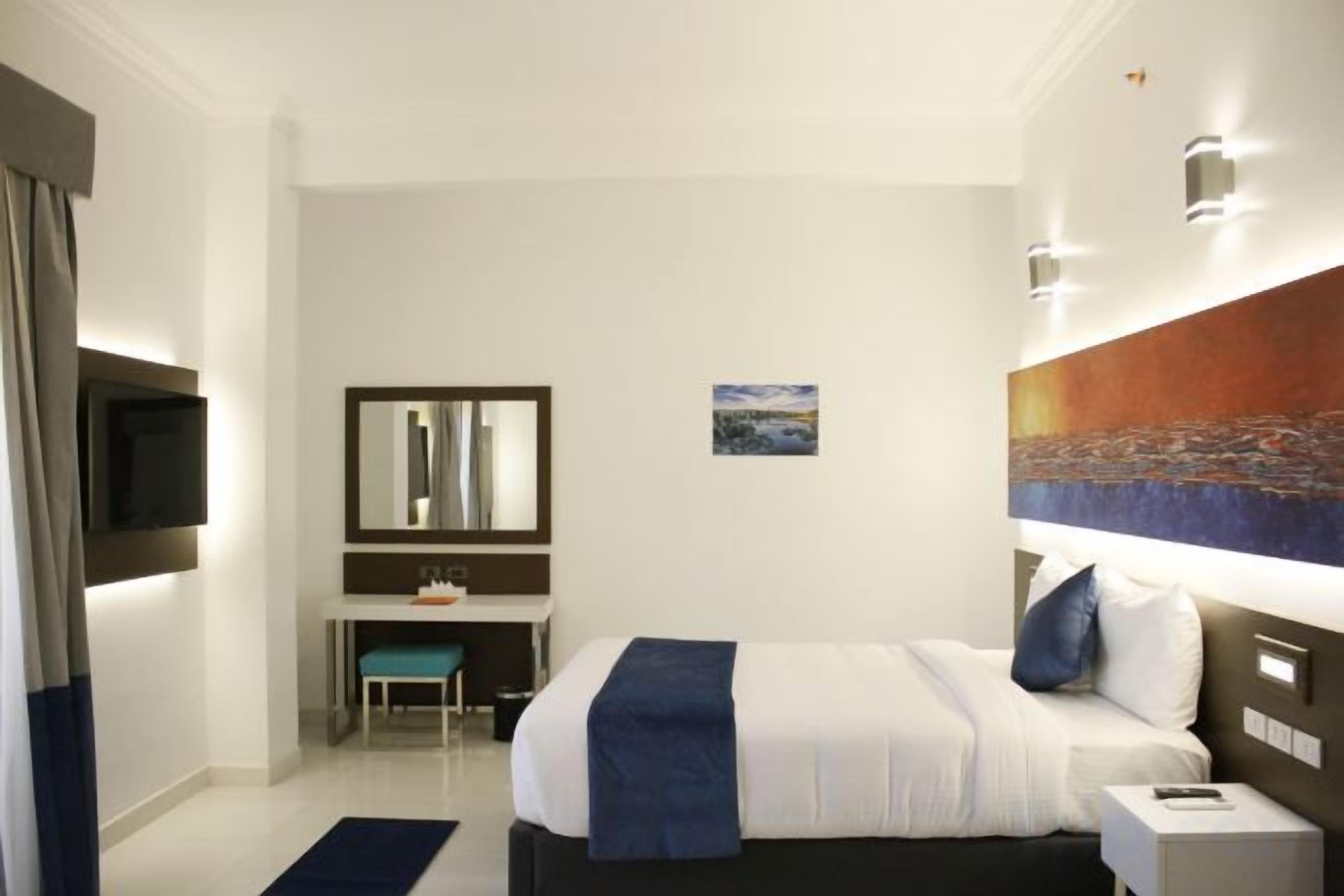 A hotel room with a bed, bedside table, desk, chair, and a television.