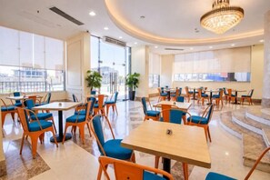 A hotel dining area with multiple tables and chairs, large windows, and a chandelier. - Gloria Aqua Park (Aswan)
