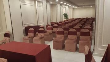 Une salle de conférence avec des rangées de chaises et de tables, des murs blancs et un plafond doté d’un éclairage encastré.