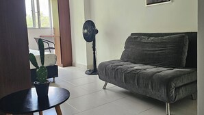 A living room with a grey sofa, a standing fan, a cactus plant, and a framed picture on the wall. - La Estación Lofts By LGH (Medellín)