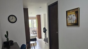 A hallway with a clock, a framed artwork, a desk, and a chair. - La Estación Lofts By LGH (Medellín)