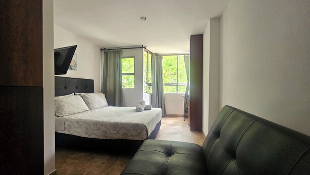 A modern bedroom with a bed, a sofa, and a TV mounted on the wall. - La Estación Lofts By LGH (Medellín)