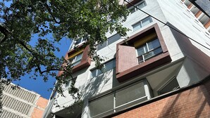 A multi-story building with a brick facade, large windows, and a tree in the foreground. - La Estación Lofts By LGH (Medellín)