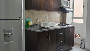 A kitchen with dark wooden cabinets, a stainless steel refrigerator, a microwave, and a gas stove. - La Estación Lofts By LGH (Medellín)