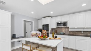 A modern kitchen with white cabinetry, a central island with seating, and a breakfast spread.