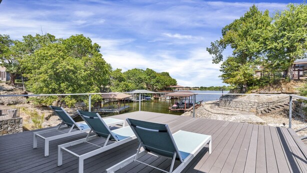 A wooden deck with lounge chairs overlooking a lake, surrounded by trees and a dock area.