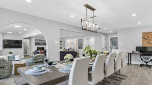 A modern dining area with a long table, white chairs, and a chandelier.