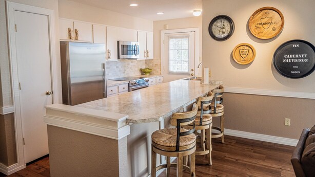 A kitchen with a central island, bar stools, a refrigerator, microwave, and wine-themed wall decor. - Rustic cabin in charming Ruidoso (Ruidoso)