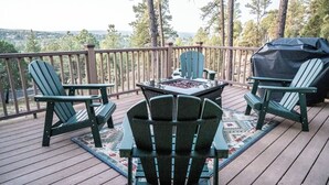 A wooden deck with Adirondack chairs, a table with a fire pit, and a grill. - Rustic cabin in charming Ruidoso (Ruidoso)