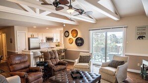 A spacious living room with leather chairs, a tufted ottoman, and a view of the kitchen and balcony. - Rustic cabin in charming Ruidoso (Ruidoso)