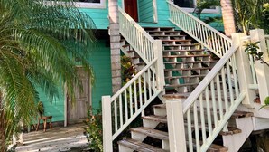 Una casa turquesa con una escalera que lleva a la entrada, rodeada de palmeras.