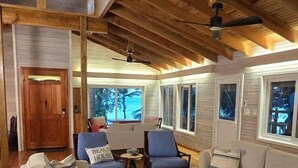 Amplia sala de estar con vigas de madera, un sofá, sillas, una mesa de centro y vistas a palmeras a través de amplios ventanales.