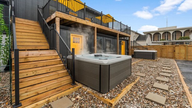 Ein Wellnessbereich mit Whirlpool, Holzterrasse und einem Gebäude mit gelber Tür und Balkon.