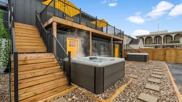 Un área de spa con hidromasaje, terraza de madera y un edificio con puerta amarilla y balcón.