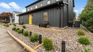 Ein modernes, zweistöckiges Gebäude mit dunkler Fassade, einer gelben Tür und einem gepflegten Garten mit Kieswegen und niedrigen Sträuchern.