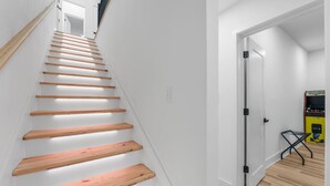 Eine Treppe mit Holzbeschlägen und weißen Wänden führt zu einem Raum mit einer Tür und einer Spielmaschine.