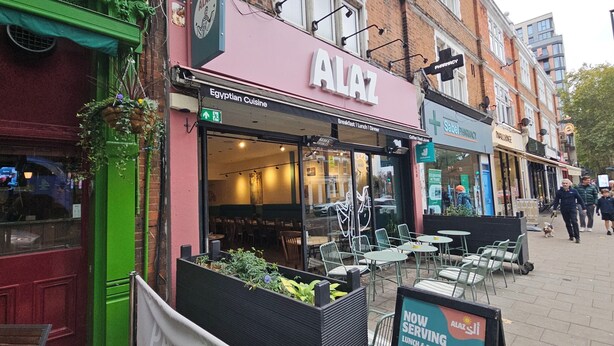 A restaurant named 'ALAZ' with outdoor seating and a sign indicating it serves Egyptian cuisine.