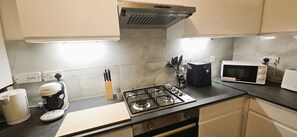 A modern kitchen with a gas stove, microwave, toaster, and a coffee maker. - Chiswick Residence (London)