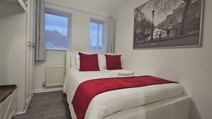 A bedroom with a bed, two windows, a radiator, and a painting on the wall.