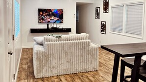 Un saló modern amb un sofà blanc, una televisió de pantalla plana i un terra de fusta.