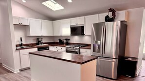 Une cuisine moderne avec des meubles blancs, un îlot central, des appareils en acier inoxydable et un plan de travail en bois.