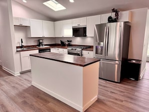 A modern kitchen with white cabinetry, a central island, stainless steel appliances, and a wooden countertop.