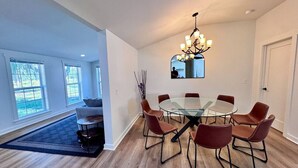 Une salle à manger moderne avec une table en verre, des chaises en cuir, un lustre et de grandes fenêtres.