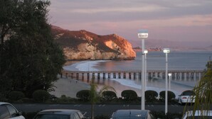 Vista costera con un muelle que se adentra en el agua, rodeado de árboles y coches estacionados.