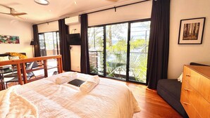 A hotel room with a bed, a desk, a chair, a dresser, and large windows with a view of greenery. - The Palm Tree Loft, close to shops and lake (Green Point)