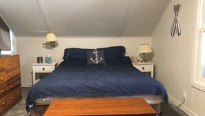 A bedroom with a large bed, two nightstands, a wooden dresser, and a window. - Enjoy fall colors 2-bedroom cottage on Long Lake  Dundee. WI   on the water (Campbellsport)