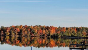 A calm lake with a dock and chairs, surrounded by trees with autumn foliage. - Enjoy fall colors 2-bedroom cottage on Long Lake  Dundee. WI   on the water (Campbellsport)