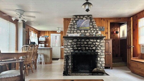 A cozy cabin interior with a stone fireplace, wooden walls, a dining area with a table and chairs, and a kitchen with a microwave and refrigerator. - Enjoy fall colors 2-bedroom cottage on Long Lake  Dundee. WI   on the water (Campbellsport)