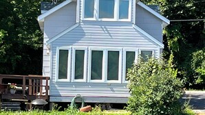 A two-story house with a gable roof, large windows, and a front porch. - Enjoy fall colors 2-bedroom cottage on Long Lake  Dundee. WI   on the water (Campbellsport)