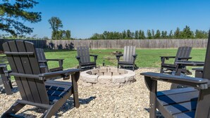 Un jardin avec des fauteuils Adirondack disposés autour d’un foyer en pierre.